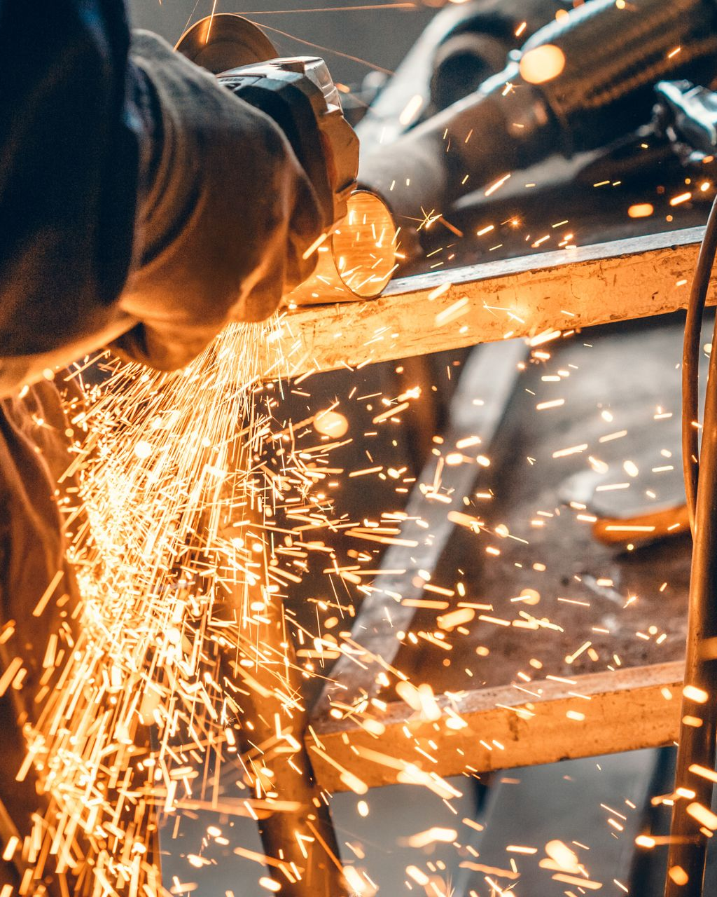 Une personne meule du métal avec une meuleuse d'angle, créant des étincelles dans un atelier.