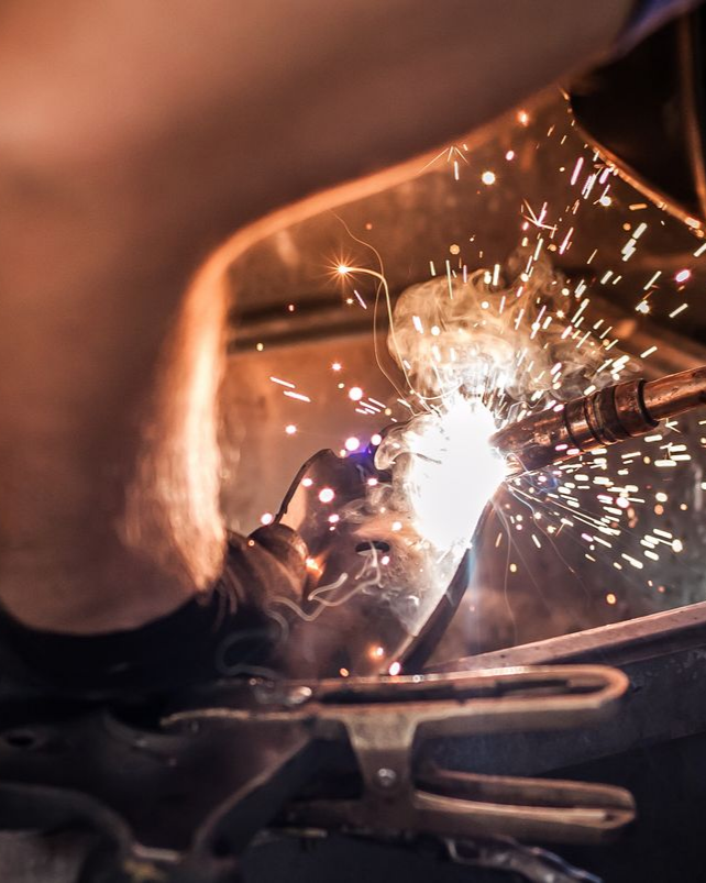 Soudeur utilisant une torche, avec des étincelles volant dans une zone faiblement éclairée.
