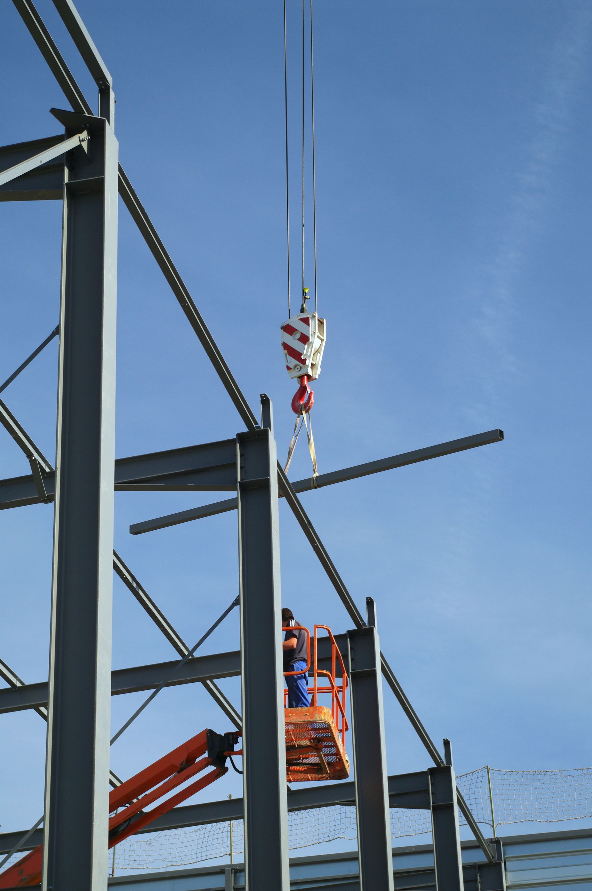 Des ouvriers du bâtiment sur un ascenseur, plaçant une poutre métallique avec une grue contre un cadre en acier, ciel bleu.