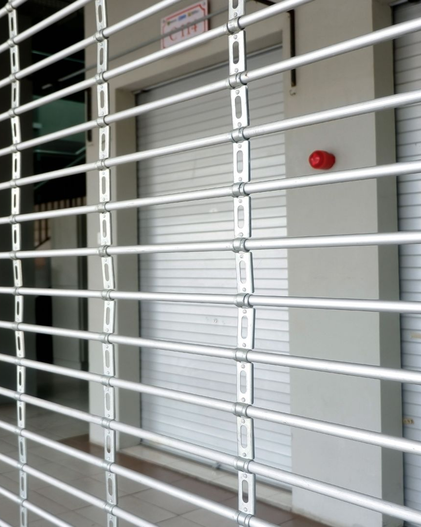 Grille de sécurité en métal au-dessus d'une porte blanche fermée, avec une lumière rouge sur le mur.