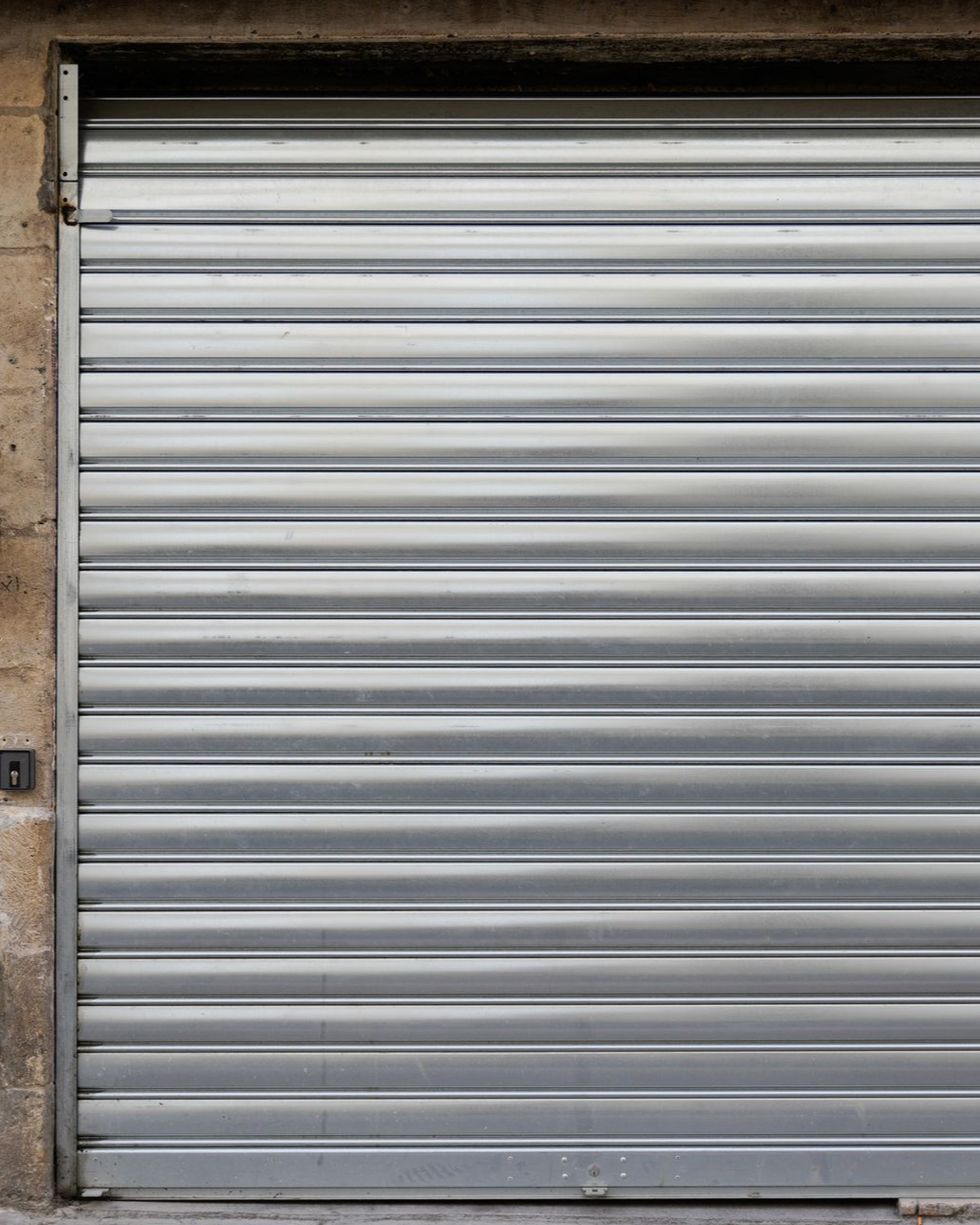 Porte enroulable en métal argenté, fermée, dans un mur en béton beige.