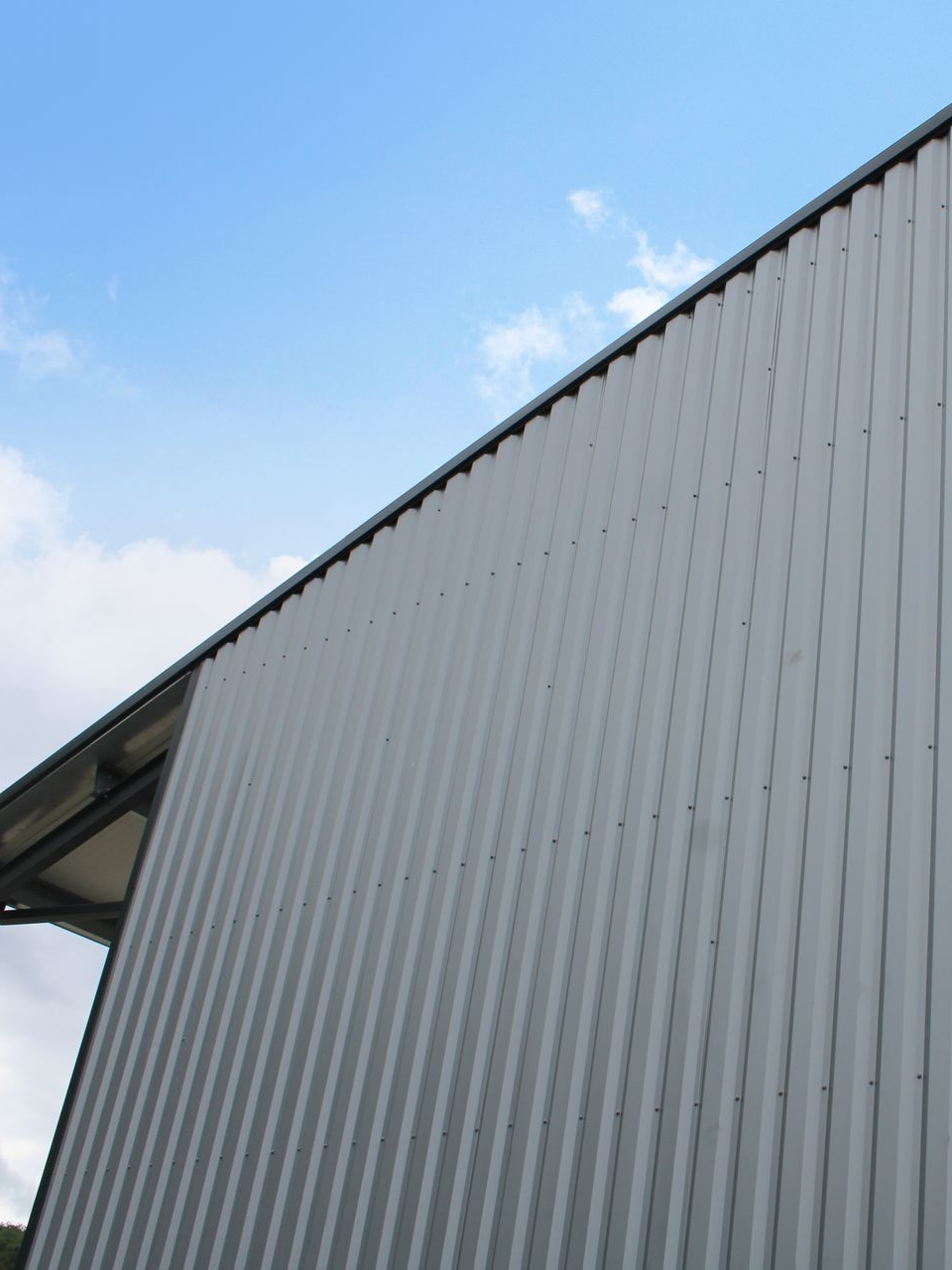 Bâtiment en tôle ondulée grise sous un ciel bleu avec des nuages.