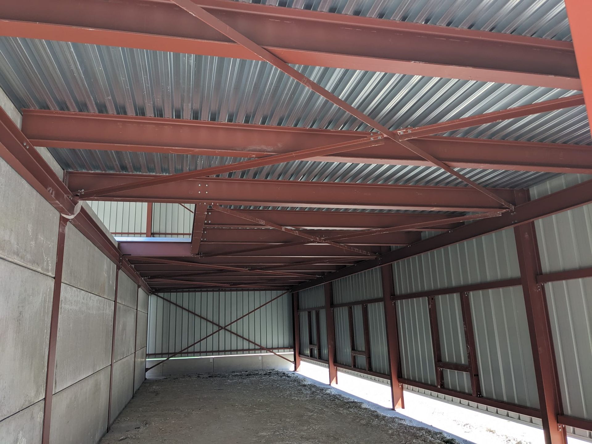 Intérieur d'un bâtiment en construction. On aperçoit des poutres métalliques et une toiture en tôle ondulée.