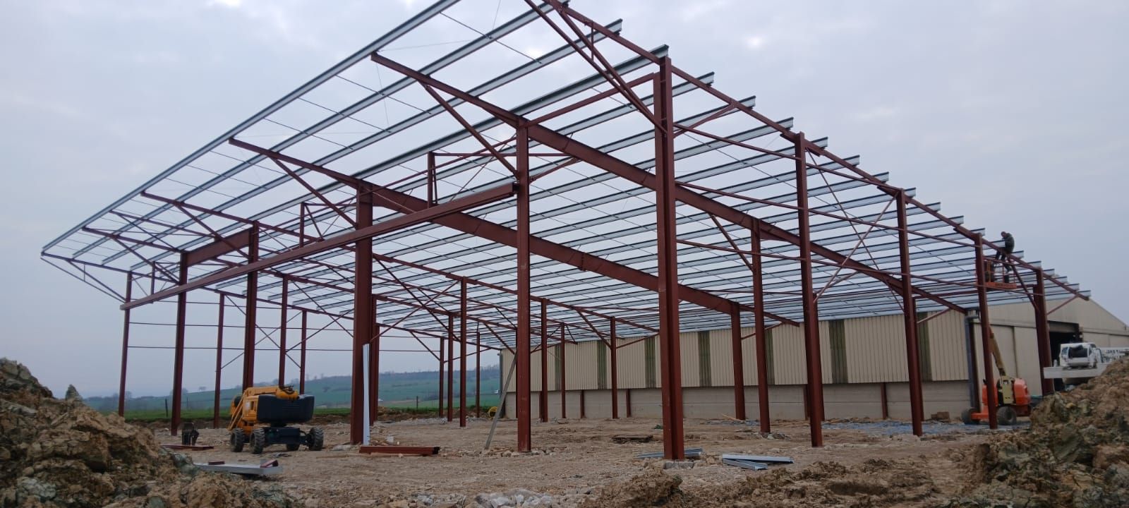 Construction d'une structure en acier sous un ciel nuageux. Ouvriers et machines visibles sur le chantier.