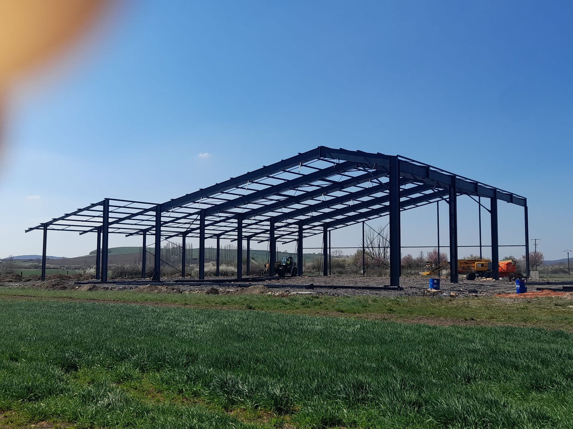 Structure en acier d'un grand bâtiment en construction dans un champ, contre un ciel bleu.