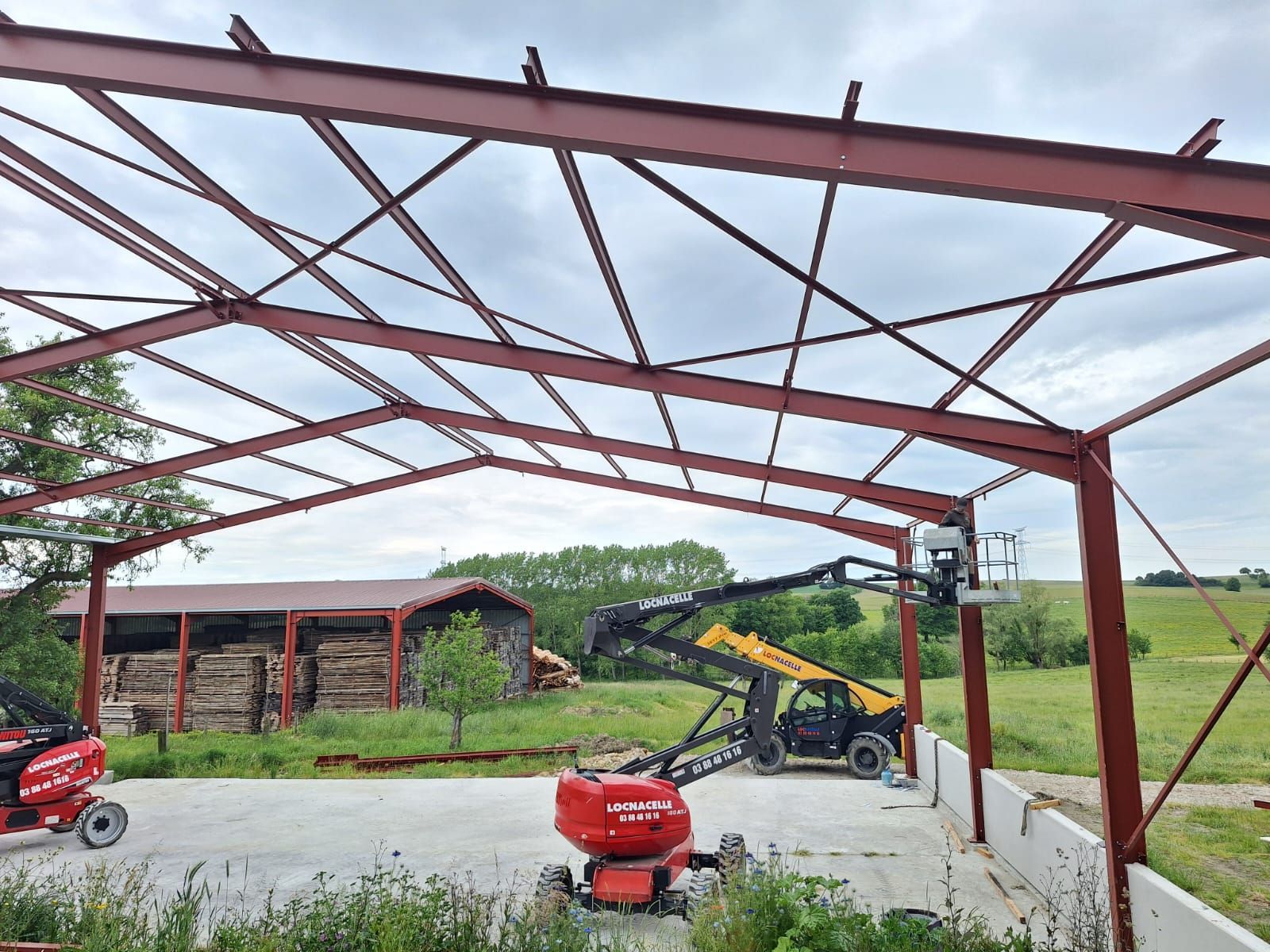 Construction d'un bâtiment à ossature métallique. Structure métallique rouge, deux ascenseurs, fondations en béton, environnement rural.
