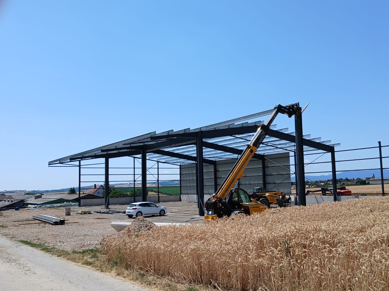 Structure en acier d'un bâtiment en construction par une journée ensoleillée avec un tracteur travaillant sur le toit.