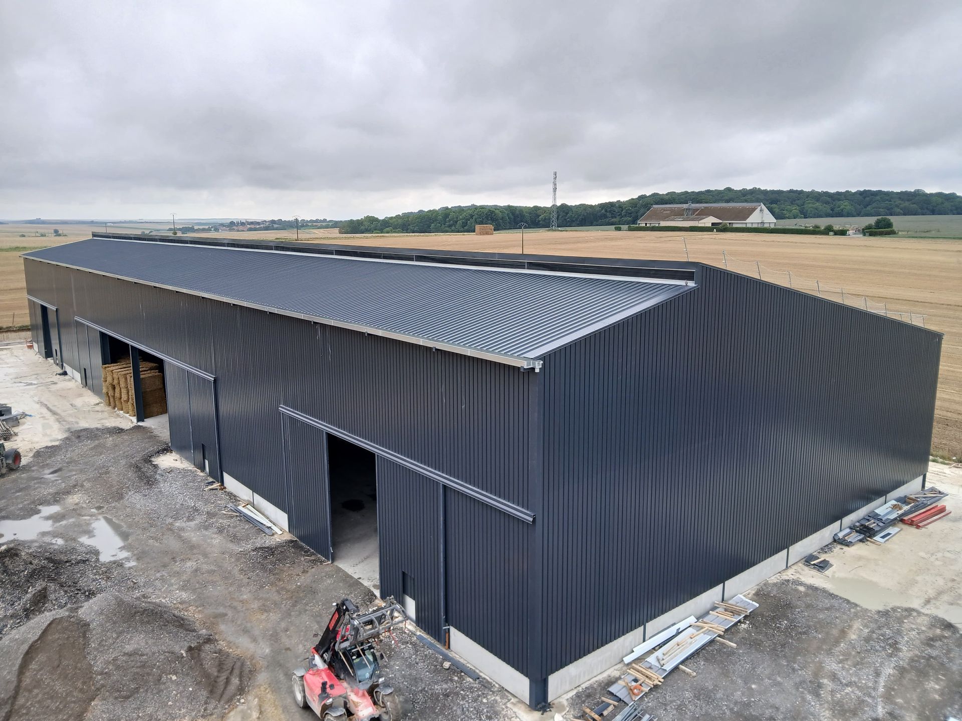 Bâtiment agricole en métal gris foncé avec portes coulissantes, ciel couvert.