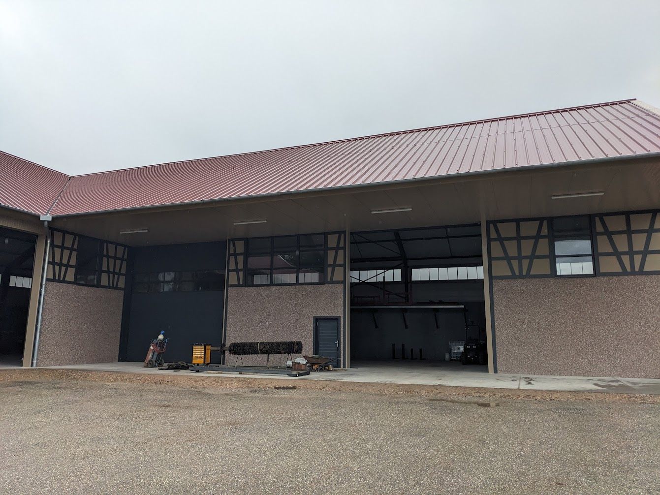 Bâtiment avec baies ouvertes, toit rouge et façade en briques par temps nuageux.