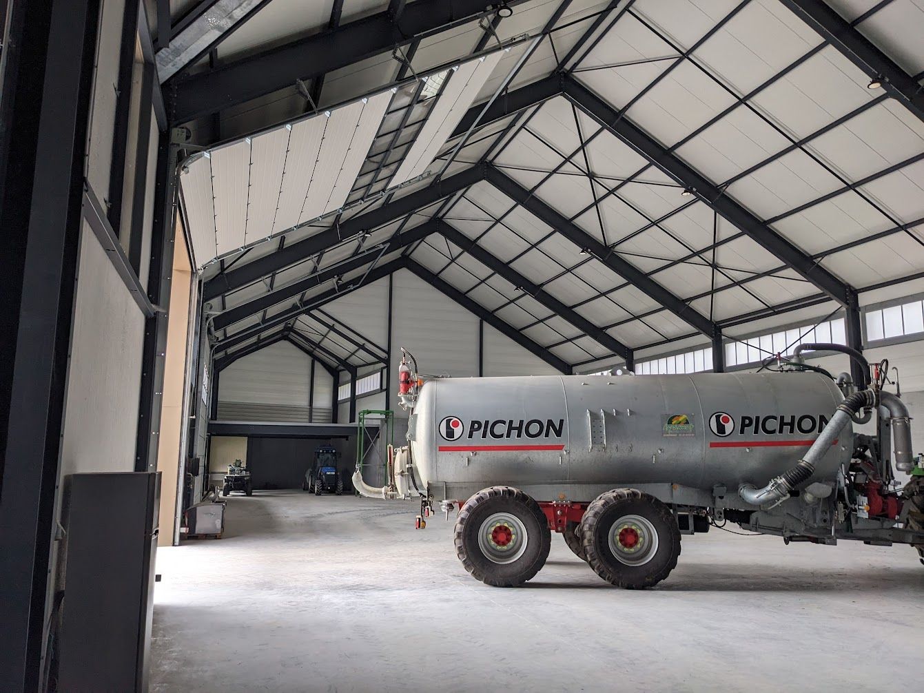 Grande remorque citerne argentée dans une grange aux murs blancs avec un cadre en métal noir.