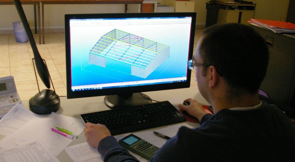 Un homme devant un ordinateur, utilisant un logiciel de CAO pour concevoir la structure d'un bâtiment.