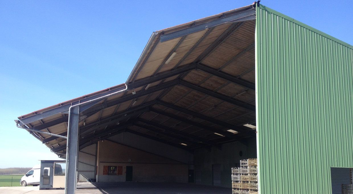 Grange recouverte de métal vert avec toit en pente, côté ouvert et ciel bleu.