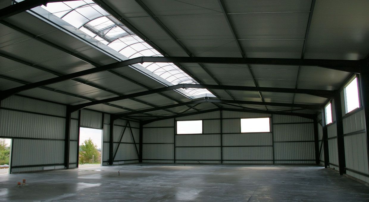 Structure de toit en métal blanc recouverte de neige, surplombant un champ enneigé sous un ciel nuageux.