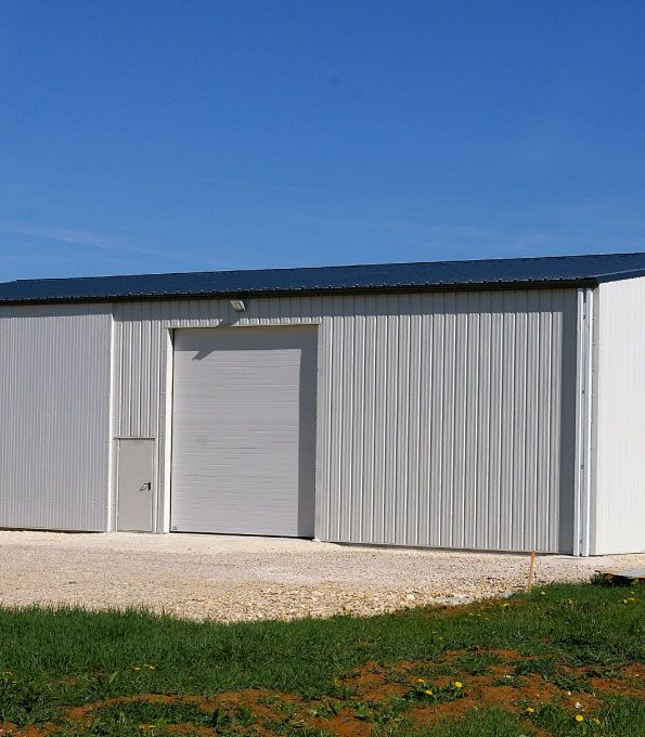 Entrepôt en métal vert avec une porte de garage grise sous un ciel bleu.