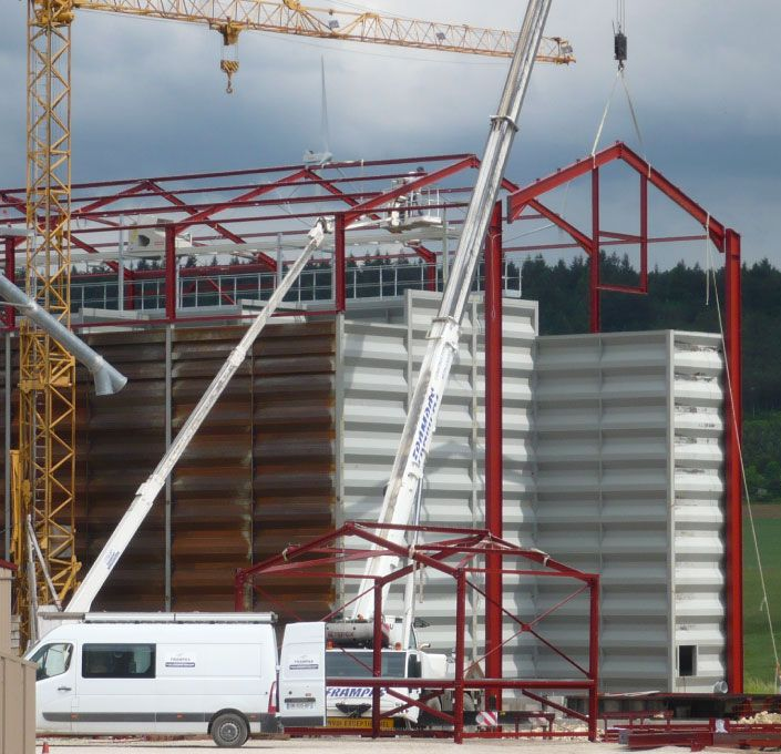 Vue depuis un puits de lumière sous un ciel bleu vif à travers des panneaux de verre encadrés de poutres blanches et grises.