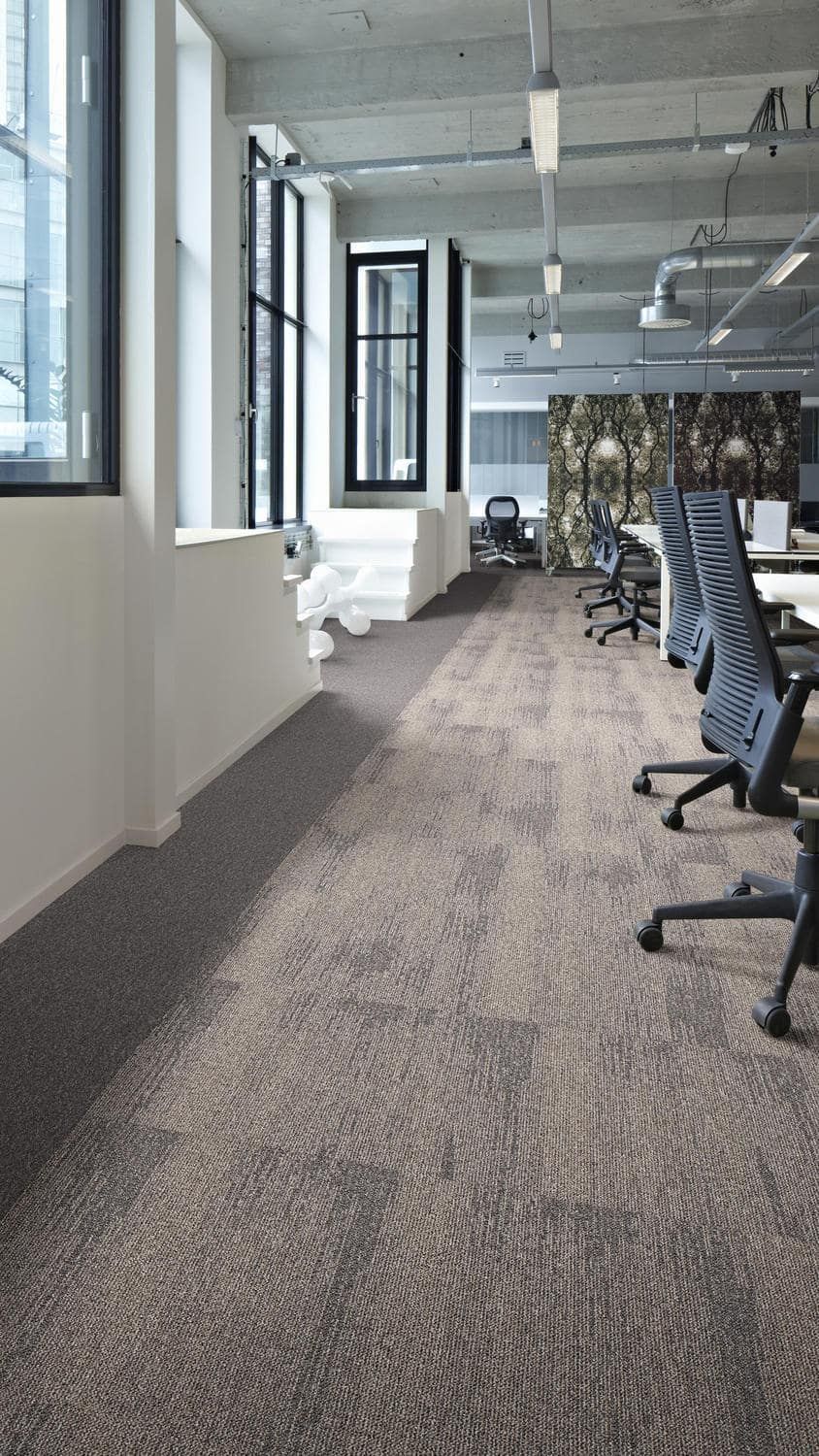 Un largo pasillo en una oficina con piso alfombrado y sillas.