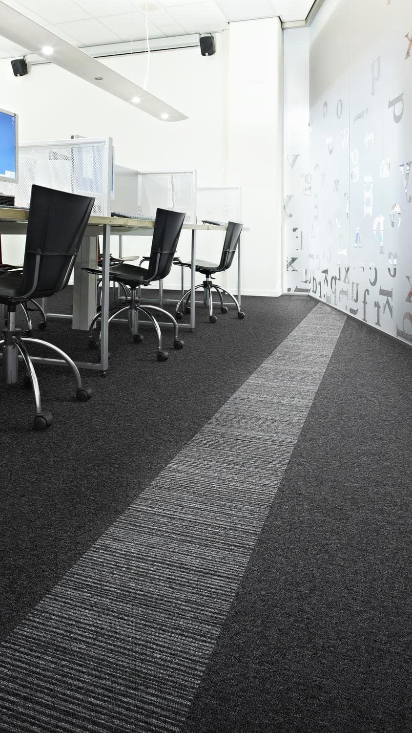 Una fila de escritorios y sillas en una oficina con piso alfombrado.