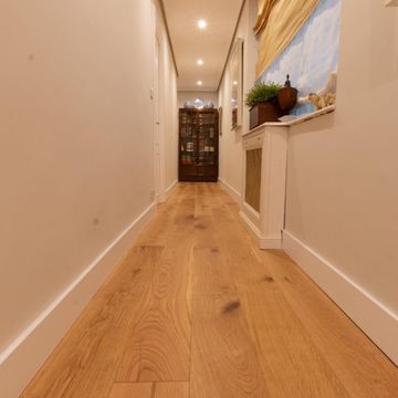 Un largo pasillo con pisos de madera y paredes blancas.
