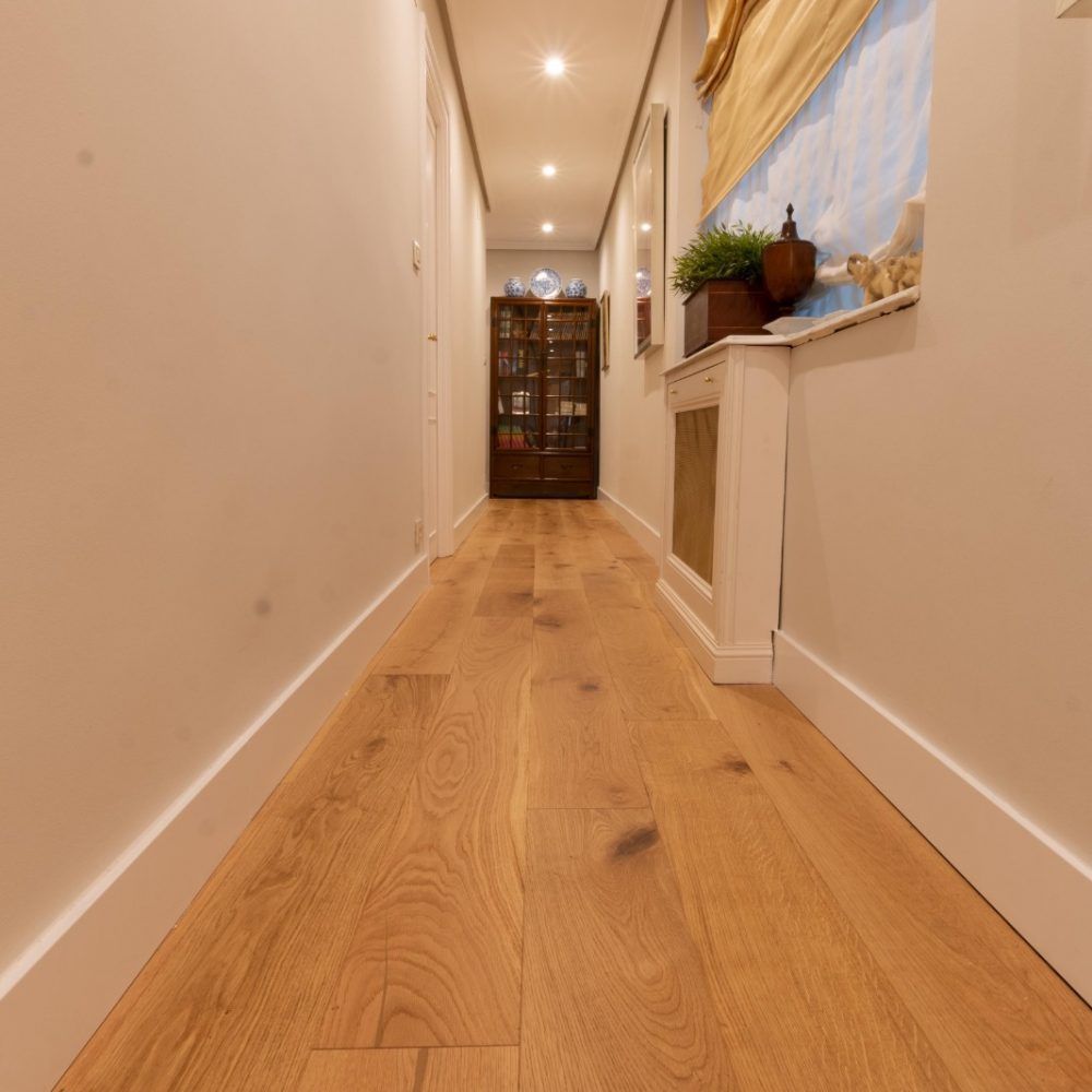 Un largo pasillo con suelos de madera y paredes blancas.