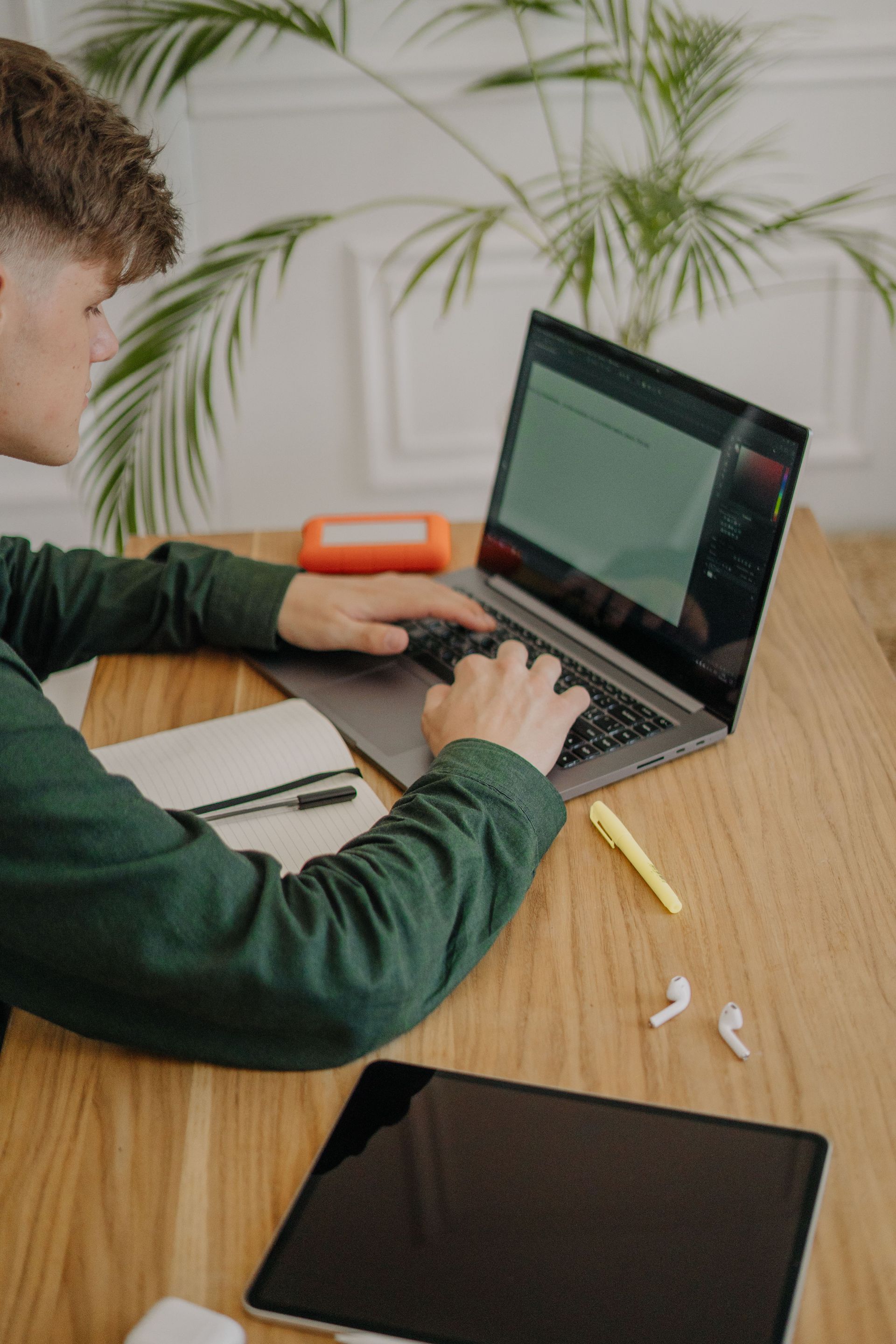 Personne utilisant un ordinateur portable à une table en bois, avec un carnet et un crayon.