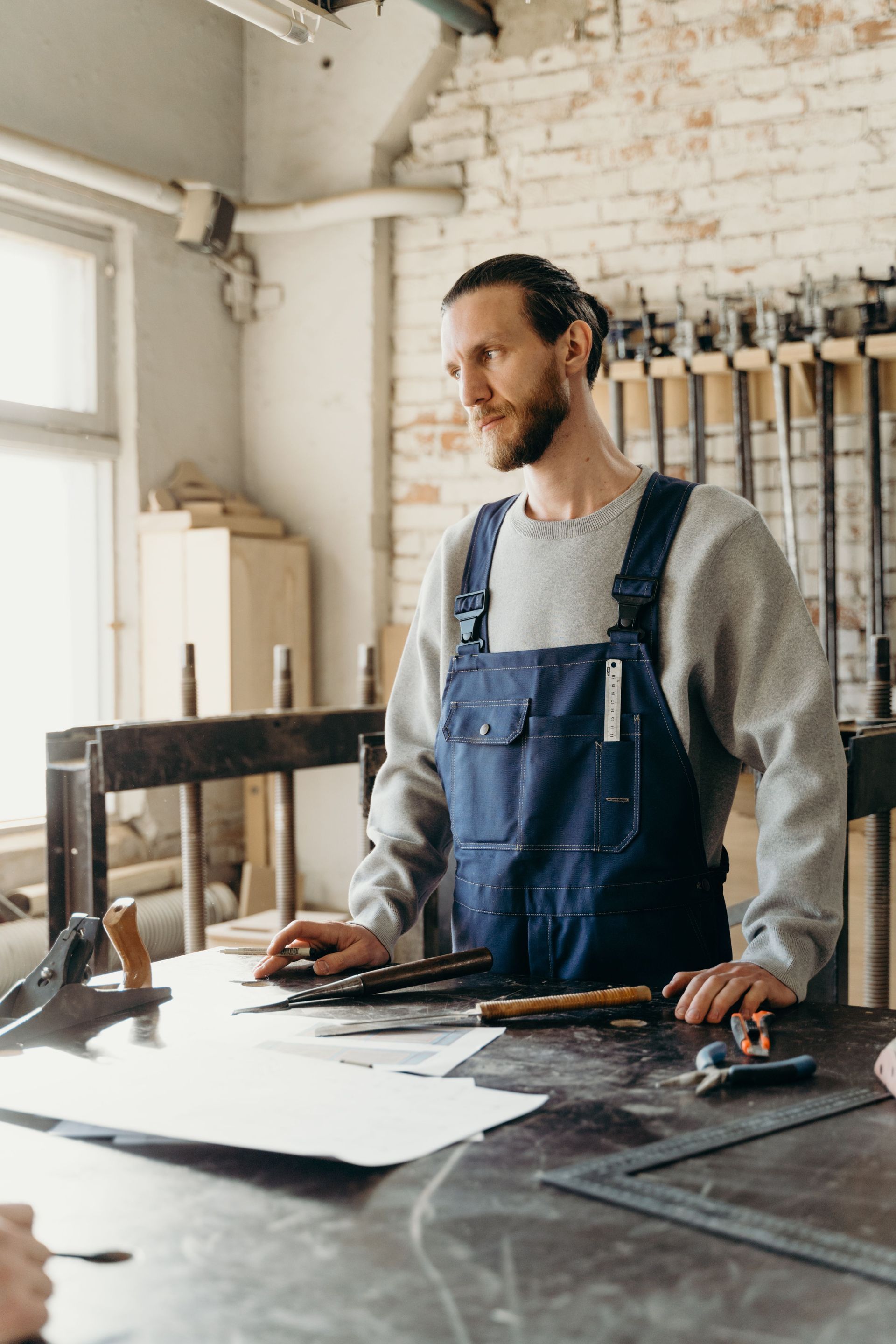 Ouvrier en bleu de travail, debout à un établi couvert d’outils et de documents dans un atelier