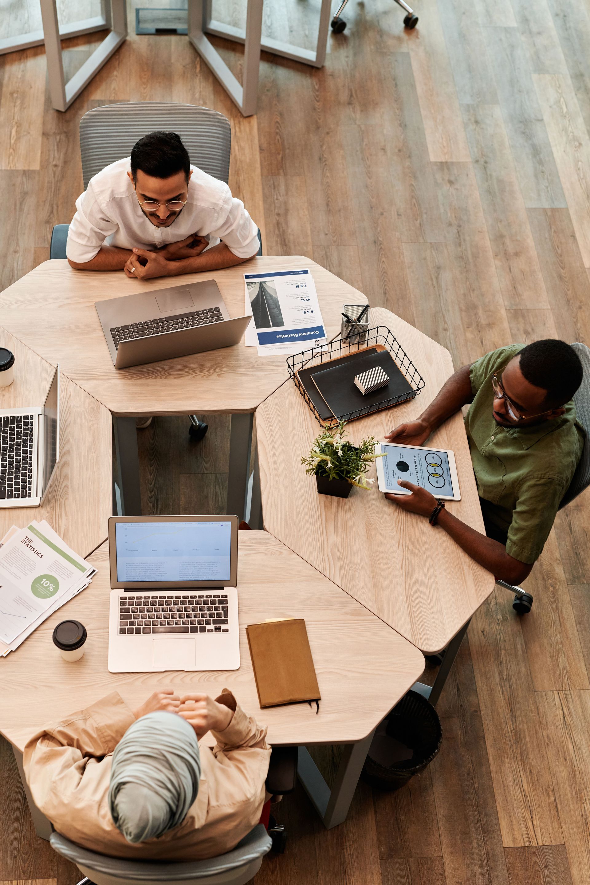 Quatre personnes collaborent autour d’une table hexagonale, avec des ordinateurs portables et des documents.