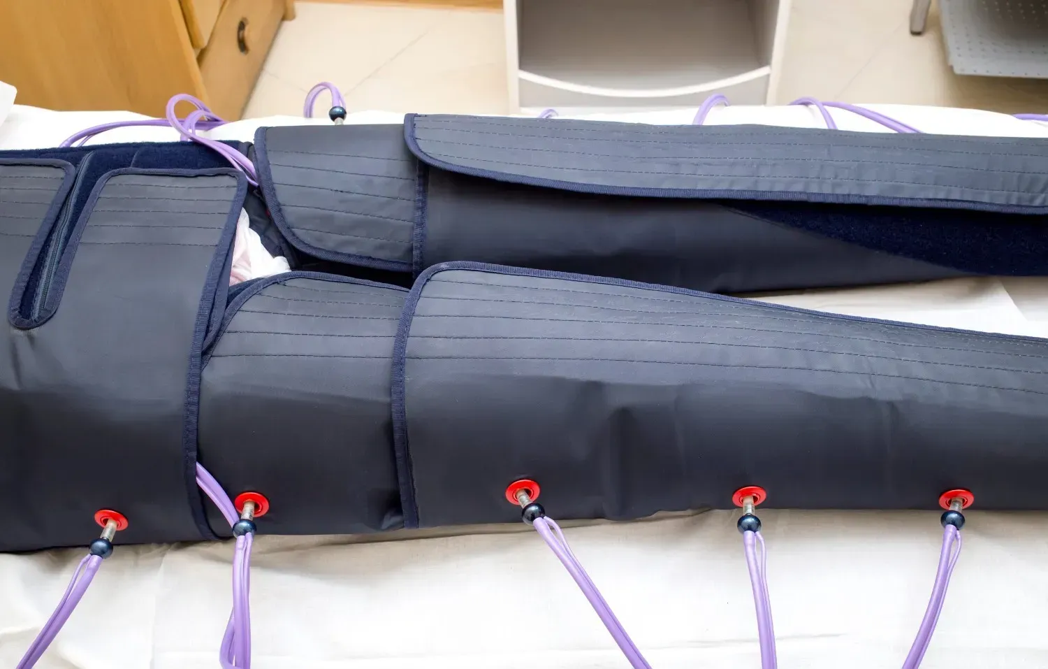 Una persona tumbada con mangas de compresión azul oscuro en las piernas, conectadas mediante tubos morados a un dispositivo de tratamiento.