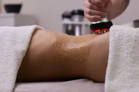 Se está utilizando un dispositivo que emite luz roja para realizar un tratamiento cosmético en el abdomen de una persona, que está cubierto de gel.