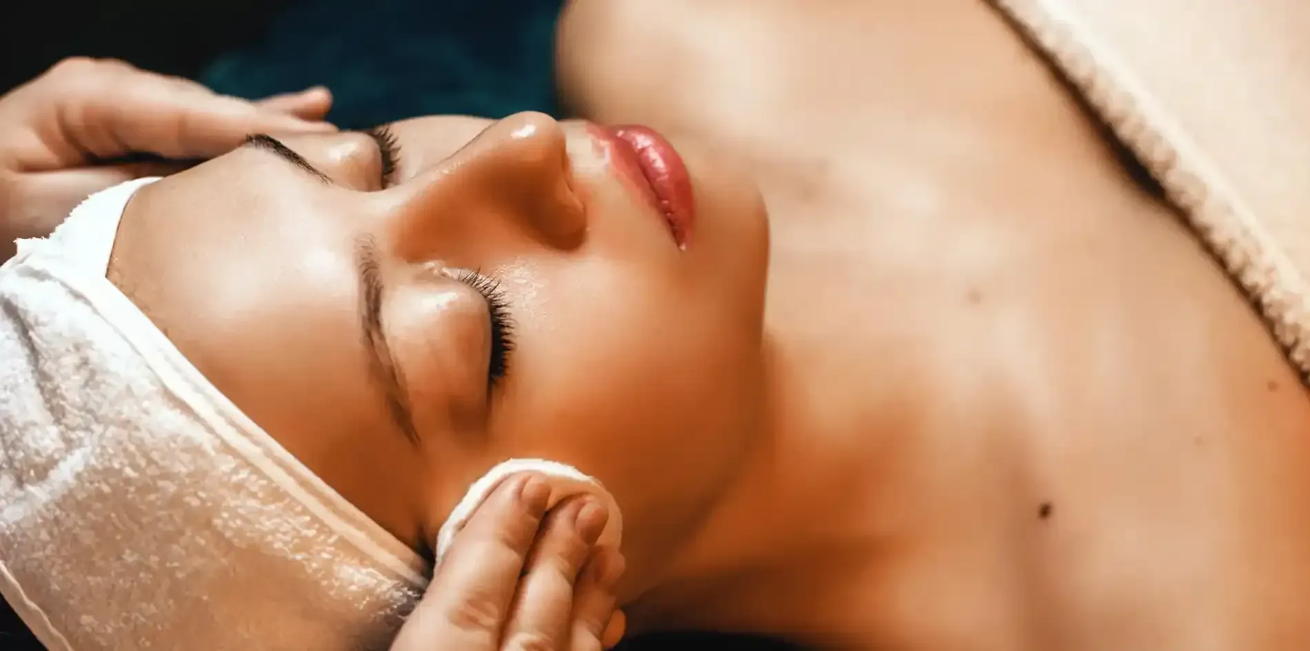 Persona recibiendo un relajante masaje facial con una toalla envuelta alrededor de la cabeza.