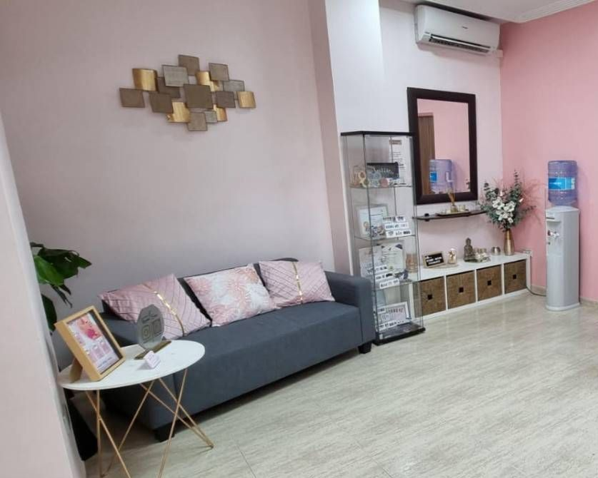 Un sofá gris con cojines estampados, una mesita blanca, decoración de pared, una vitrina y un dispensador de agua en una habitación rosa.