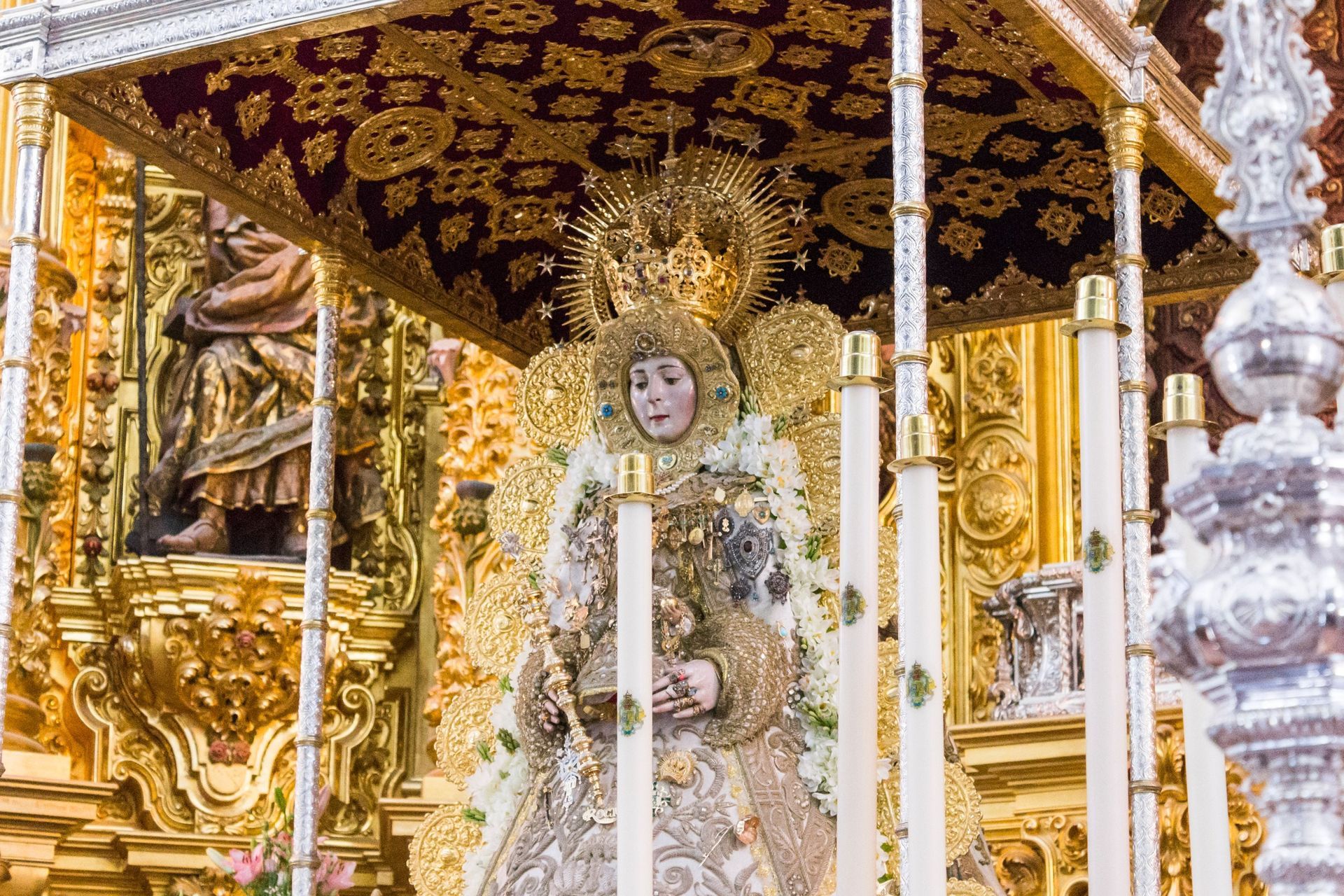 Anuncio inmobiliario: Estatua de la Virgen María, blanca y dorada, con flores rosas