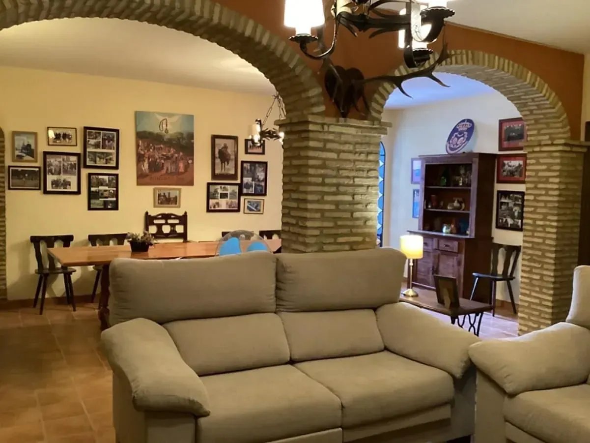 Sala de estar beige con sofá color canela, arcos de ladrillo y comedor con cuadros.