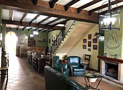 Sala de estar rústica con vigas de madera, escalera y chimenea. Paredes verdes y muebles de cuero.