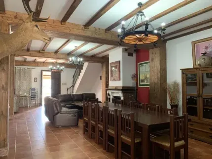 Amplio comedor con una gran mesa, vigas de madera a la vista y una cabeza de ciervo montada.