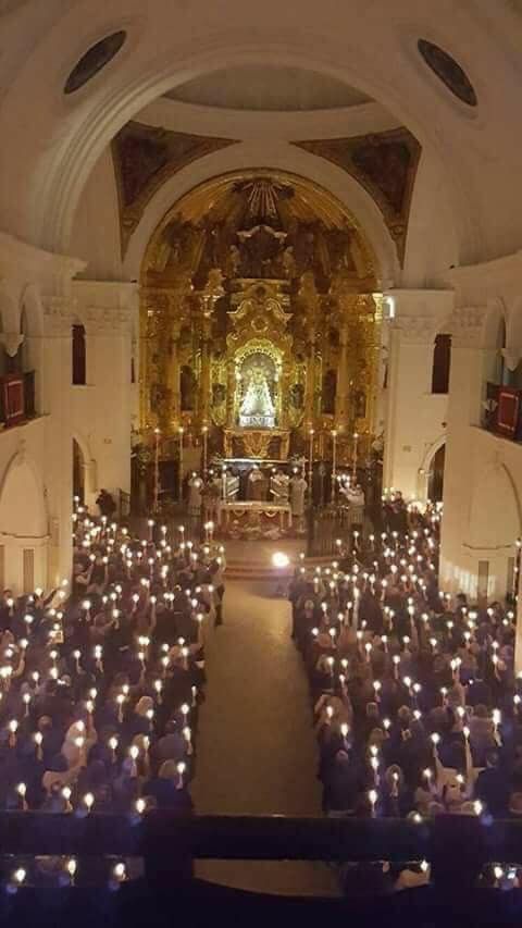 Interior de una iglesia iluminada por velas, una gran multitud mirando hacia el altar.