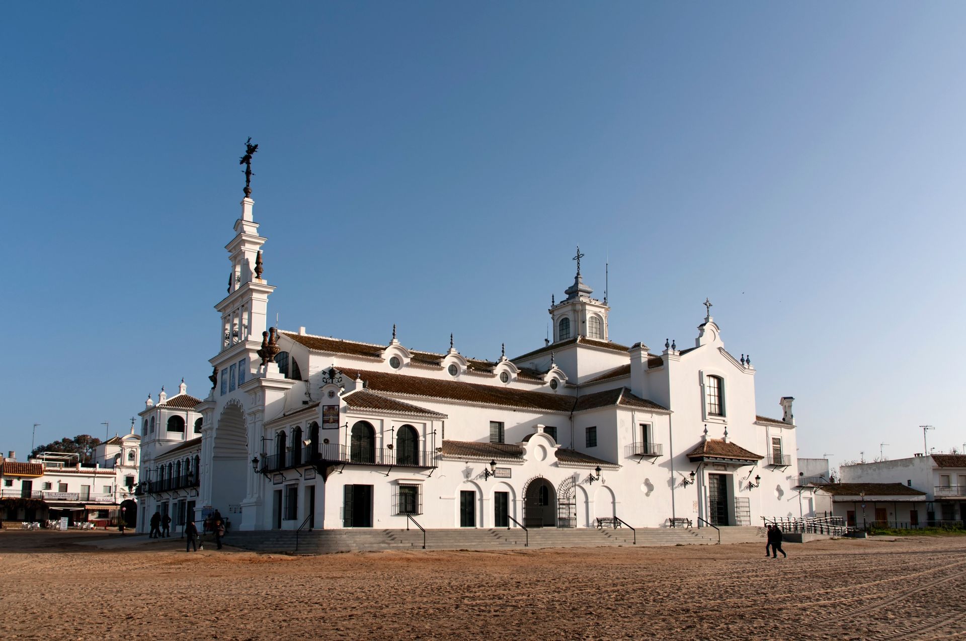 Iglesia blanca con una torre alta contra un cielo azul claro en España; la gente camina cerca.