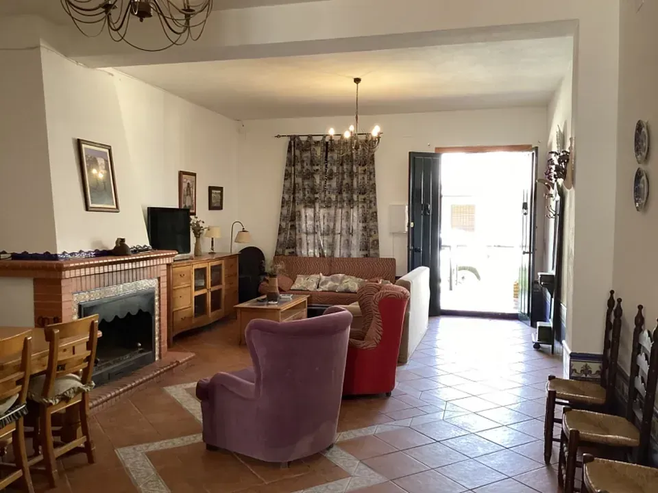 Sala de estar con chimenea, sofás y sillas. Puerta abierta al exterior.