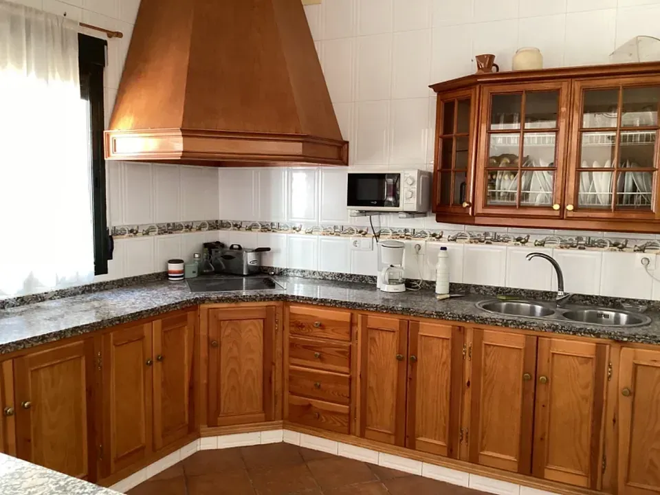 Una cocina con gabinetes de madera, encimeras de granito y microondas, con luz natural proveniente de la ventana.