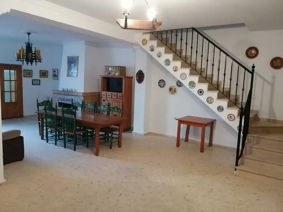 Amplio comedor con mesa larga, sillas y escalera adornada con platos decorativos.