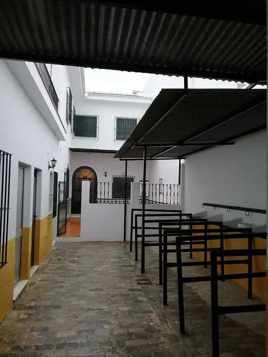 Un patio estrecho con paredes blancas, pasarela cubierta y aparcabicicletas metálicos, posiblemente en España.