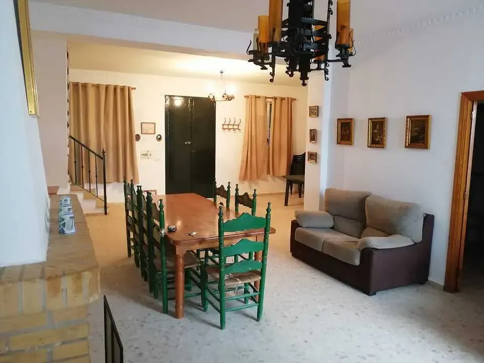 Comedor con mesa larga, sillas verdes, sofá, obras de arte y lámpara de araña.