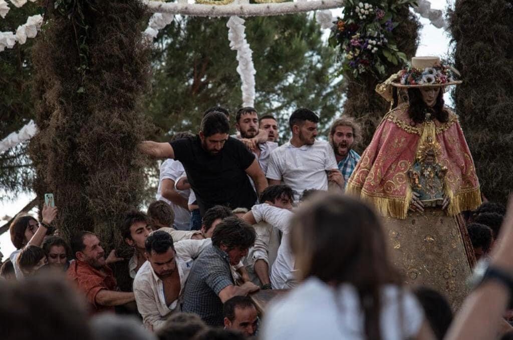 Personas portando una figura religiosa entre la multitud, probablemente durante un festival. Luz solar, al aire libre.
