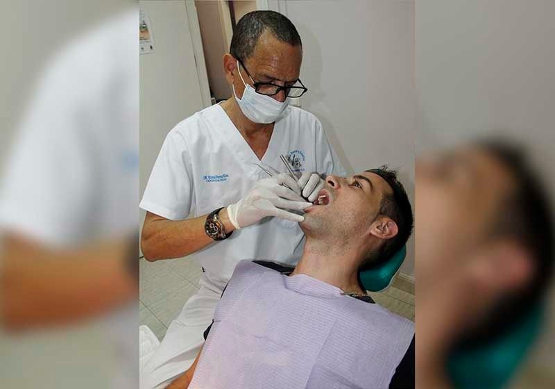 Un hombre está sentado en una silla dental mientras un dentista examina sus dientes.
