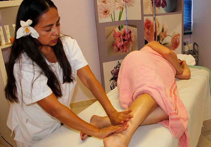 Una mujer está dando un masaje a una mujer envuelta en una toalla rosa.