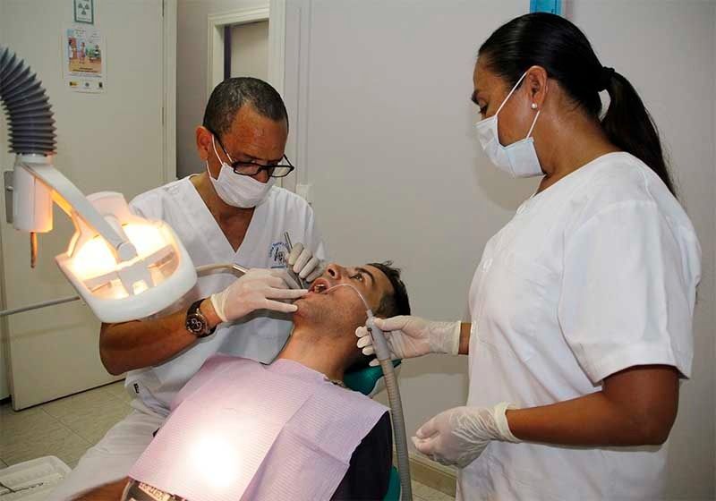 Un hombre está siendo examinado por dos dentistas en un consultorio dental.