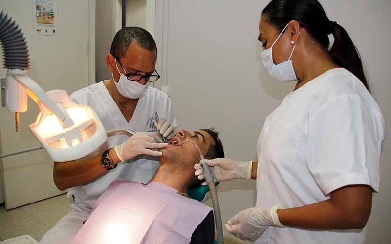 Un hombre está siendo examinado por dos dentistas en un consultorio dental.