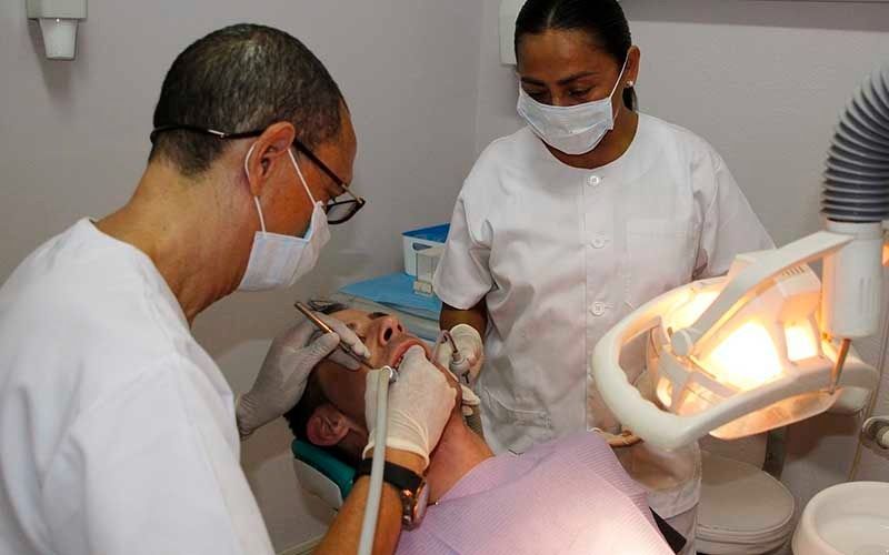 Un hombre está siendo examinado por dos dentistas en un consultorio dental.