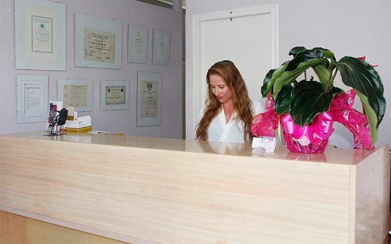 Una mujer sentada en un mostrador de recepción con una planta delante de ella.