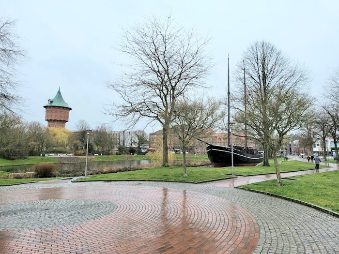 In der Mitte eines Parks steht ein Boot, im Hintergrund ist ein Wasserturm zu sehen.