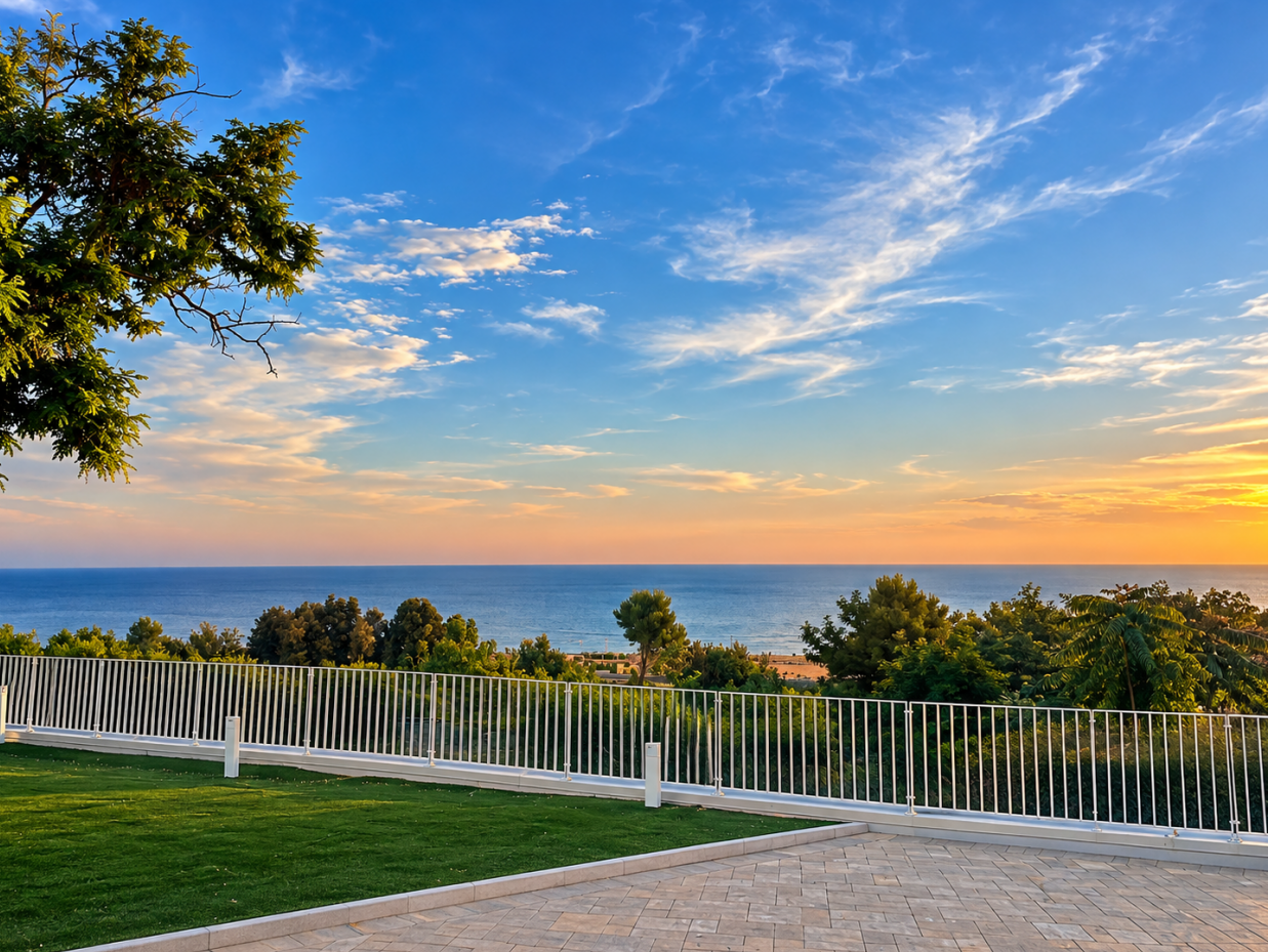 Sunset over a calm lake with a white fence, green lawn, trees, and blue sky with wispy clouds